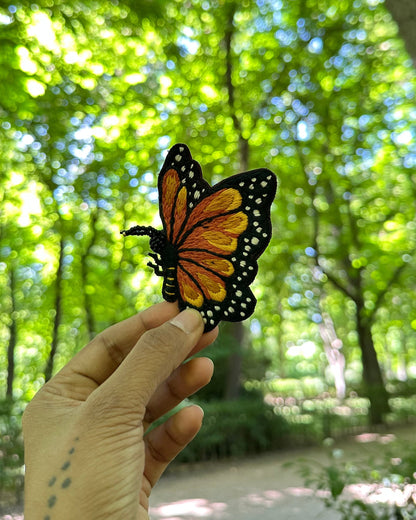Butterfly brooch held by a hand with a forest background