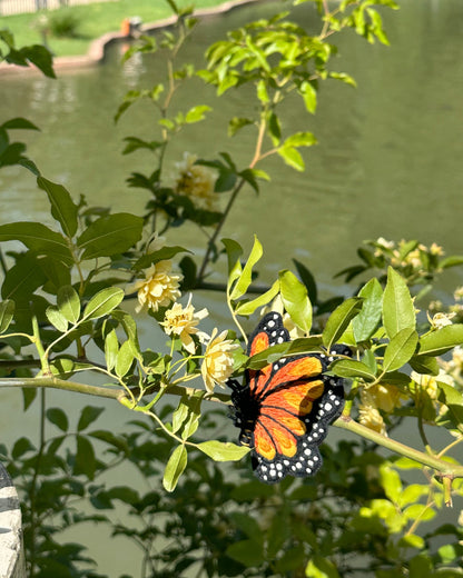 Butterfly brooch on a branch with a park pond and people in the background