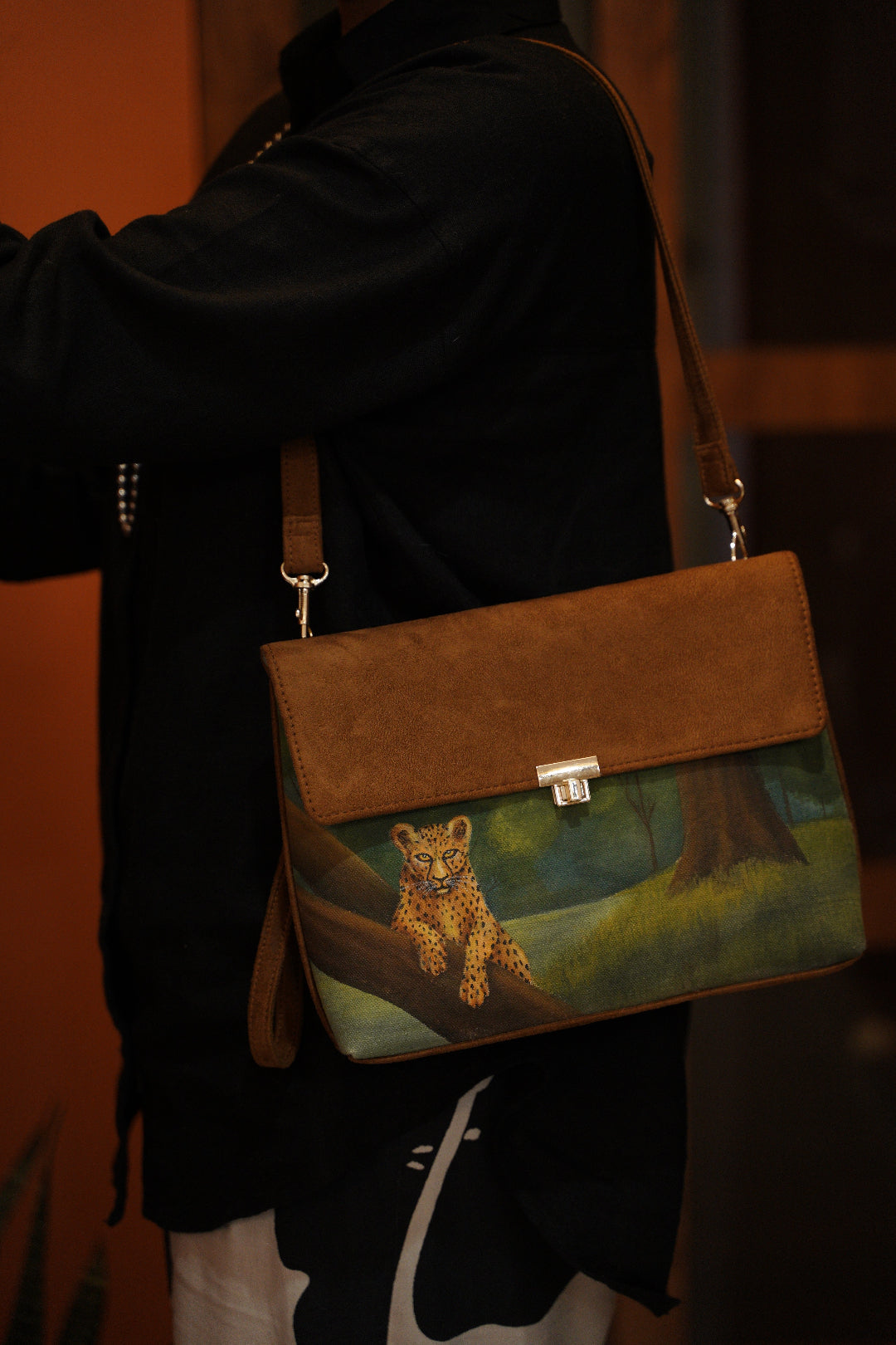 Brown leather bag with a hand-painted art of a leopard in a wild forest landscape on a dark background